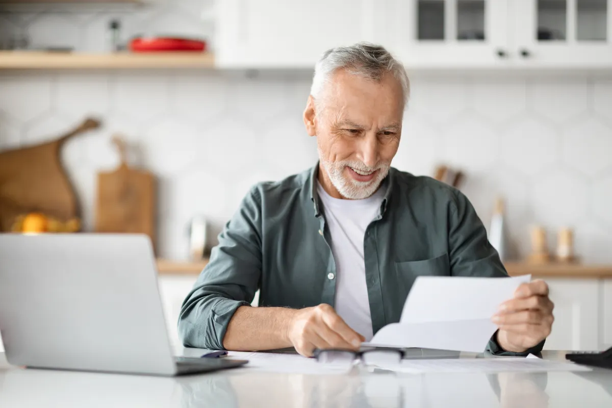 Homme relisant un courrier devant son ordinateur, dans sa cuisine