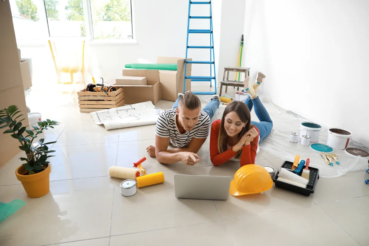 Jeune couple préparant des travaux dans son logement, ordinateur portable ouvert