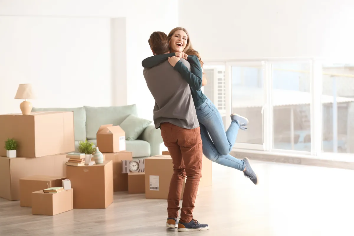 Jeune couple dans la pièce de son premier logement, entouré de cartons